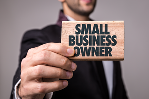 man in suit holding wood block that says small business owner